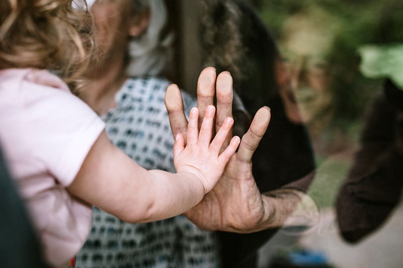 Young girl with hand against grandpa on glass